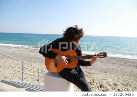 Man Plays Classical Guitar On The Beach Near The Sea In Summer 125260420