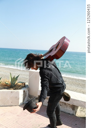 Street Artist Takes a Bow After Playing Classical Guitar on the Beach Near Ocean 125260435