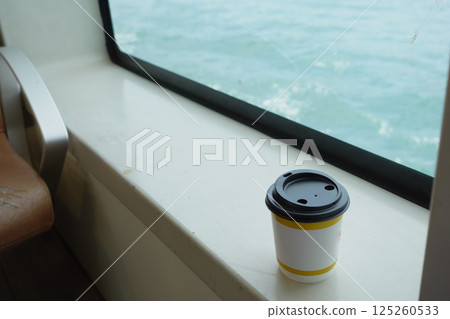 Coffee cup resting on a windowsill with ocean view 125260533