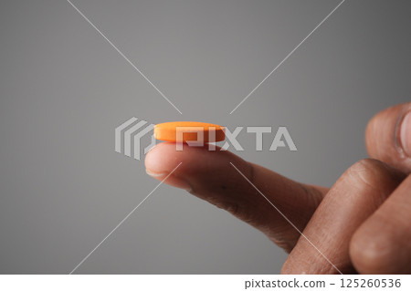 Balancing a bright orange disk on fingertip in a soft-lit setting 125260536