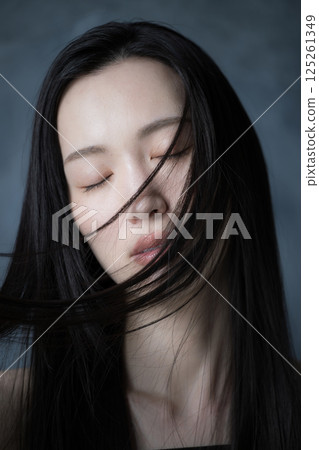 A woman with her eyes closed and a serious expression showing her hair flowing against a gray background, showing her determination and strong will A woman with her eyes closed and a serious expression showing her hair flowing against a gray background, showing her determination and strong will 125261349