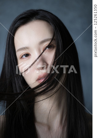 特寫鏡頭中，一位表情嚴肅的女子，在灰色背景下，她的頭髮飄揚，顯示出她的決心和堅強的意志。 125261350