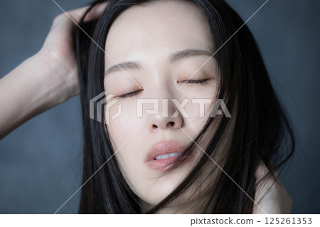 A woman with her eyes closed and a serious expression showing her hair flowing against a gray background, showing her determination and strong will 125261353