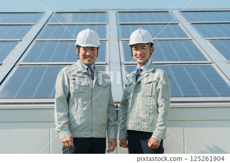 An engineer in work clothes from an electric power company or electrical contractor standing in front of a solar power generation/solar panel (clean energy) 125261904