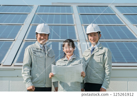 An engineer in work clothes from an electric power company or electrical contractor standing in front of a solar power generation/solar panel (clean energy) An engineer in work clothes from an electric power company or electrical contractor standing in front of a solar power generation/solar panel (clean energy) 125261912