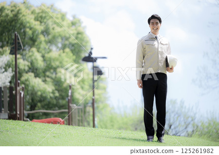 Full body wearing work clothes and holding a helmet outdoors in fresh greenery Image of construction management, work site, etc. Full body wearing work clothes and holding a helmet outdoors in fresh greenery Image of construction management, work site, etc. 125261982