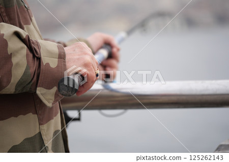 Fisherman holding rod on a pier during calm waters 125262143