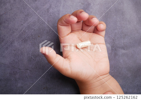 Child's hand holding a dietary supplement capsule in natural light 125262162