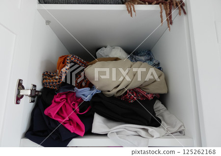 Clothes are disorganized in a cluttered closet shelf 125262168
