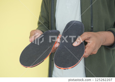 Unique insoles held casually against a yellow backdrop 125262207