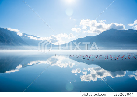 Mountains with clouds and their reflection in the still waters of the sea, separated by a strip of fog in winter morning Bay of Kotor in Montenegro 125263044