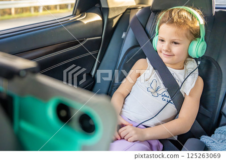 Little girl with tablet and headphones in the car during travel on vacation. Entertainment in the transport for child 125263069