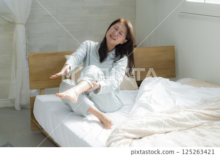 Senior woman in bedroom with leg cramps 125263421