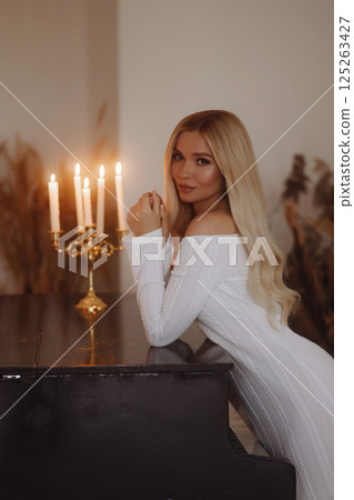 Elegant woman in white dress leaning on black piano. Loft interior. 125263427