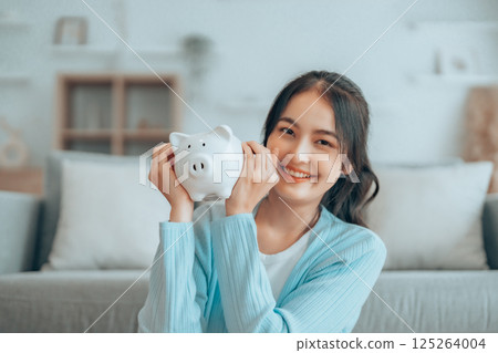 Young Asian woman holding piggy bank and sitting on the floor at home 125264004