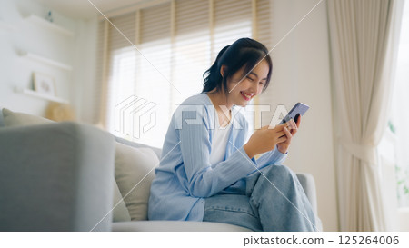 Smiling pretty young Asian woman sitting on cozy couch 125264006