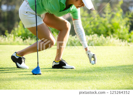 Asia sporty woman put golf ball on tee with club in golf course Asia sporty woman put golf ball on tee with club in golf course 125264352