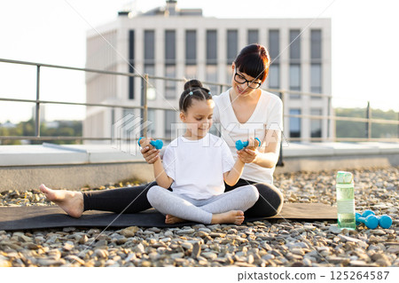 Mother and her young daughter exercising together on rooftop, bonding through fitness activities with dumbbells, promoting healthy family lifestyle and active habits for well-being and positive energy Mother and her young daughter exercising together on rooftop, bonding through fitness activities with dumbbells, promoting healthy family lifestyle and active habits for well-being and positive energy 125264587