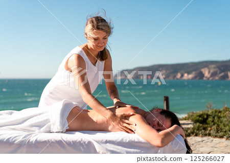 Masseur giving back massage to woman near sea at Masseur giving back massage to woman near sea at 125266027