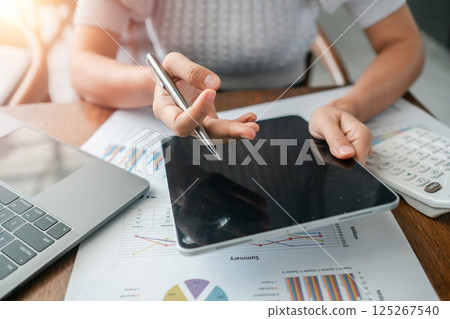 Close-up of a person using a tablet to review financial charts, surrounded by a laptop and calculator. Close-up of a person using a tablet to review financial charts, surrounded by a laptop and calculator. 125267540