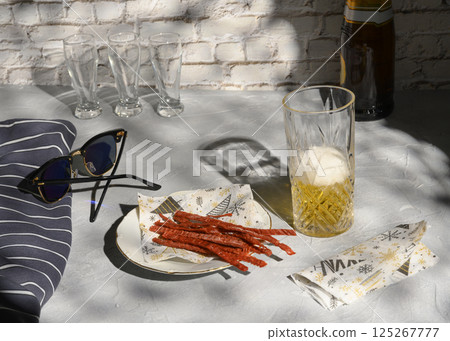 Still life with a glass of beer, fish straws, sunglasses and a vest, casting shadows from the sun Still life with a glass of beer, fish straws, sunglasses and a vest, casting shadows from the sun 125267777