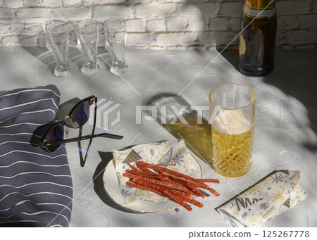 Still life with a glass of beer, fish straws, sunglasses and a vest, casting shadows from the sun 125267778