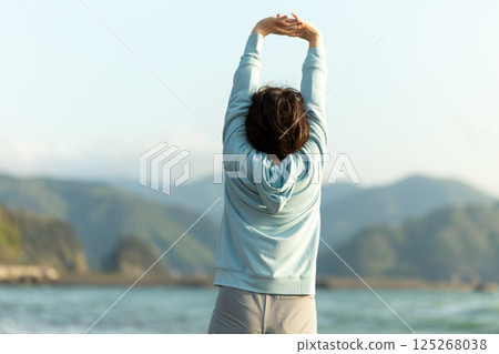 Middle-aged woman doing stretching exercises on the beach in the evening 125268038