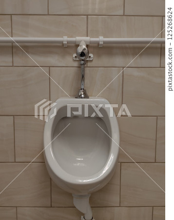 urinal in public restroom with neutral tiled walls and simple design. close up. 125268624