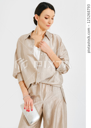 Elegant woman in stylish outfit posing confidently with clutch purse against plain backdrop 125268793
