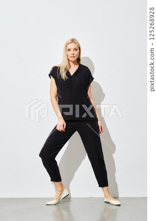 Woman wearing a black cotton outfit posing against a white wall 125268928