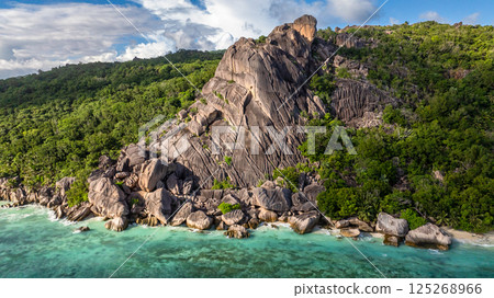Rocky coastline with lush green trees along the turquoise waters and beaches. La Digue, Seychelles. 125268966