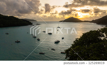 Boats anchored in a calm bay as the sun sets, with an island silhouette in the background. Seychelles, Mahe. Port Launay. 125269019