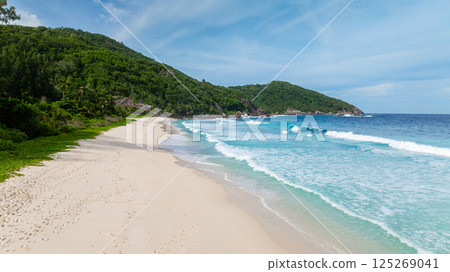A secluded beach with white sand and footprints leading towards lush greenery and turquoise waters. Seychelles, Mahe. Police Bay. A secluded beach with white sand and footprints leading towards lush greenery and turquoise waters. Seychelles, Mahe. Police Bay. 125269041