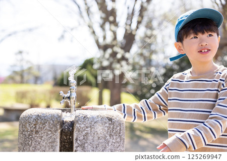 Boy drinking water from a tap in the park Boy drinking water from a tap in the park 125269947