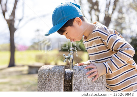 Boy drinking water from a tap in the park Boy drinking water from a tap in the park 125269948