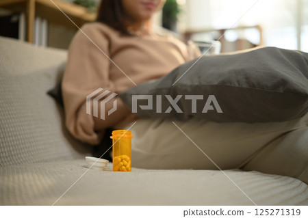 Prescription medicine bottle placed beside woman on sofa. Health care concept 125271319