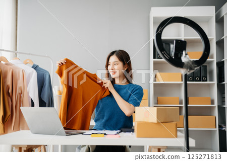 Asian lady blogger showing clothes in front of the camera to recording vlog video live streaming at her shop. Online Shopping Asian lady blogger showing clothes in front of the camera to recording vlog video live streaming at her shop. Online Shopping 125271813