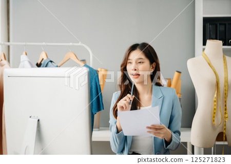 Asian young woman on desk in office of fashion designer and holds tablet, laptop and smartphone Asian young woman on desk in office of fashion designer and holds tablet, laptop and smartphone 125271823