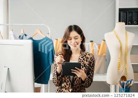Asian young woman on desk in office of fashion designer and holds tablet, laptop and smartphone Asian young woman on desk in office of fashion designer and holds tablet, laptop and smartphone 125271824