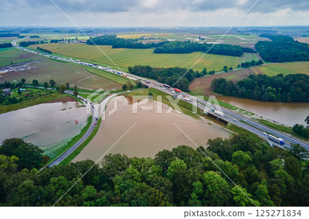 Aerial view of flooded fields and submerged rural road near busy highway. Concept of climate impact, transportation disruption and natural disaster Aerial view of flooded fields and submerged rural road near busy highway. Concept of climate impact, transportation disruption and natural disaster 125271834