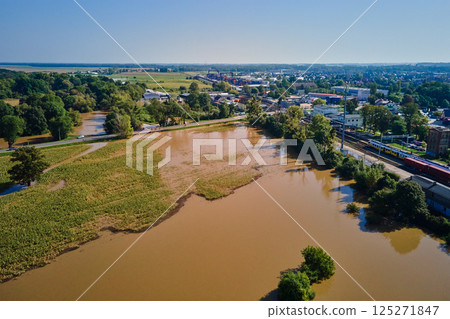 Aerial view of flooded streets, railway tracks and buildings in a suburban area. Industrial zone with floodwater after heavy rain. Concept of natural disaster, climate impact and emergency Aerial view of flooded streets, railway tracks and buildings in a suburban area. Industrial zone with floodwater after heavy rain. Concept of natural disaster, climate impact and emergency 125271847