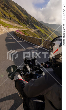 Motorcycle rider riding in Italian Alps during sunrise , handlebar view , dramatic sky . Travel and freedom, outdoor activities Motorcycle rider riding in Italian Alps during sunrise , handlebar view , dramatic sky . Travel and freedom, outdoor activities 125272178