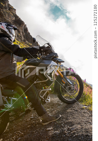 Motorcycle rider riding in Italian Alps during sunrise, dramatic sky. Travel and freedom, outdoor activities 125272180