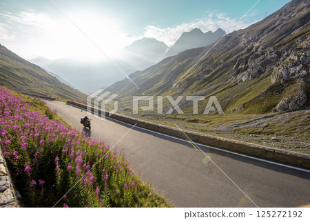 Motorcycle rider riding in Italian Alps during sunrise, dramatic sky. Travel and freedom, outdoor activities Motorcycle rider riding in Italian Alps during sunrise, dramatic sky. Travel and freedom, outdoor activities 125272192