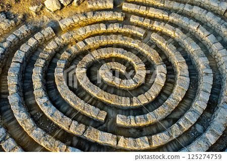 Intricate stone labyrinth nestled among greenery invites exploration and curiosity on a sunny day 125274759