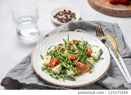 Healthy arugula salad with cherry tomatoes, mozzarella and pesto sauce on a plate 125275888