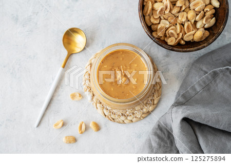 Glass jar with creamy peanut butter on grey background with scattered roasted nuts Glass jar with creamy peanut butter on grey background with scattered roasted nuts 125275894