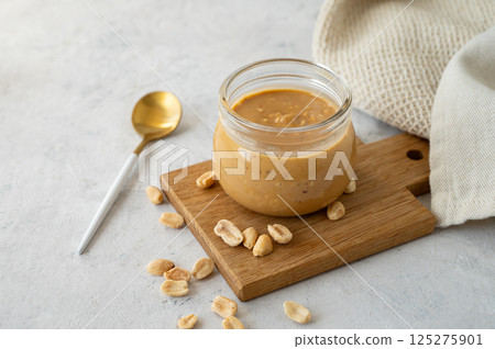 Glass jar with creamy peanut butter on a wooden board on a grey background Glass jar with creamy peanut butter on a wooden board on a grey background 125275901