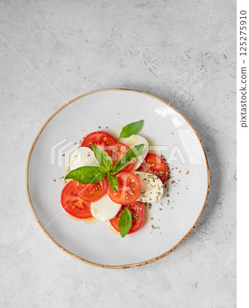 Caprese salad with sliced tomatoes, mozzarella and basil on a plate on a light background 125275910