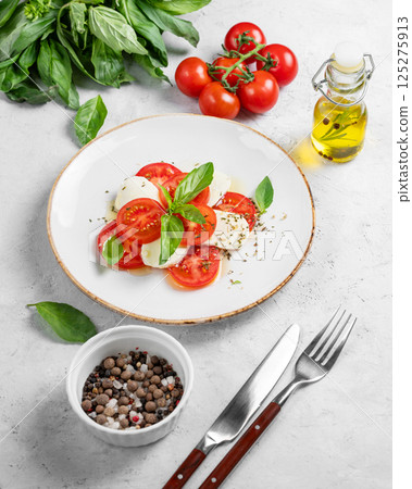 Caprese salad with sliced tomatoes, mozzarella and basil on a light background Caprese salad with sliced tomatoes, mozzarella and basil on a light background 125275913